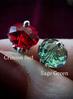 Two gemstones, one red labeled 'Crimson Red' and one green labeled 'Sage Green', held between fingers on a dark background.