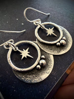 Silver earrings with star and circle designs on a dark surface