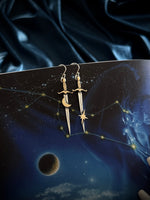 Silver sword-shaped earrings with celestial design on a dark fabric background