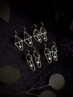Four pairs of gothic-style silver drop earrings with black stones and star details, arranged on a dark textured background with decorative leaves.