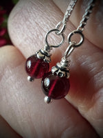 Close-up of silver earrings with red beads held between fingers.