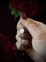Hand holding a small round pendant's backside, surrounded by red flowers on a dark background.