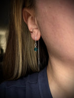 Close-up of an ear wearing a dangling earring with a blue gemstone.