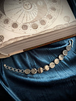 Silver bracelet on a blue fabric with an open book featuring celestial diagrams in the background