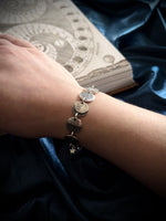 Bracelet with circular charms on a wrist, against a dark fabric background