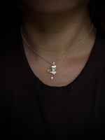 A close-up of a person's neck and chest wearing a delicate silver chain necklace with a candle-shaped pendant sitting on a small crescent moon and a star below, against a black top.