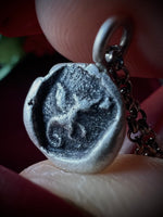 Close-up of a silver pendant with an engraved dragon design held between fingers.