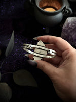 A hand holding a sterling silver crescent moon and star bangle bracelet against a dark, mystical background with a cauldron, amethyst crystal, and purple glitter.