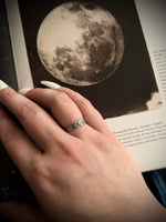 Hand with a ring on a book page featuring an illustration of the moon.
