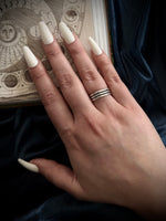 Hand with white nail polish and a ring on a dark fabric background
