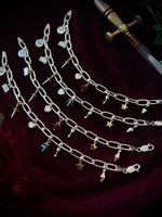 Silver chain bracelets with various mixed metal charms on a dark background with flowers and a sword.