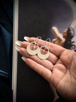 Silver moon hoop earrings held in a hand with a dark background