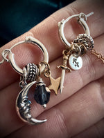 Close-up of silver hoop earrings with charms on a hand.
