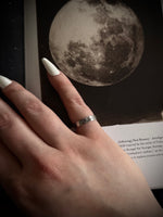 Hand with a silver ring on a surface with a moon illustration