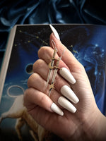 Hand holding gold star-shaped dagger earrings with a dark blue fabric background