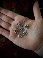 Hand holding a set of silver dragon pendants on a dark floral background.