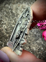 Silver necklace with an intricate pendant held by a hand on a textured surface.