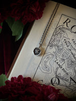 Necklace with a small silver pendant on an old map surrounded by flowers.