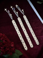 Decorative celestial bookmarks with star charms against a dark fabric background surrounded by flowers.