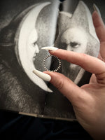 Hand holding a silver ring with a blurred background of a portrait.