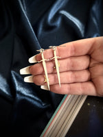 Hand holding a set of silver dagger earrings against a dark fabric background
