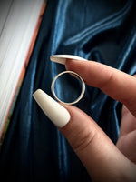 Silver ring held between fingers with a dark fabric background