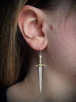 Close-up of an ear wearing a sword-shaped earring.