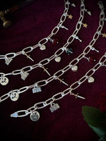 Silver chain bracelets with various mixed metal charms on a dark fabric background.