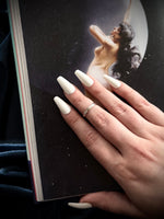 Hand with white nail polish holding a book featuring an artistic depiction of a woman.