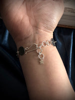 Silver bracelet with charms on a wrist against a dark background