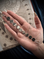 Hand holding a silver bracelet with an open book in the background