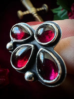 Close-up of a silver ring with red gemstones held between fingers against a dark background.