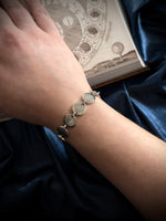 Silver bracelet on a wrist with a blue satin background