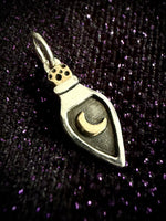 A silver pendant shaped like a teardrop vial with a gold crescent moon inside, resting on a sparkly purple textured background.