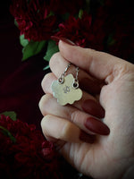 Hand holding a silver pendant's backside with a dark floral background.