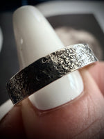 Silver ring with textured surface on a white stand