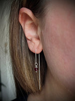 Close-up of an ear with a silver earring featuring a red gemstone.