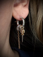Close-up of an ear with a unique earring featuring a chain and small object.
