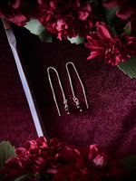 Silver chain earrings on a dark fabric background surrounded by a sword with red flowers.