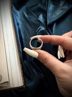 Hand holding a silver ring over a dark fabric background
