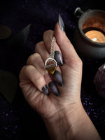 Hand holding a silver pendant with a golden tiger eye center stone.