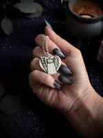 Silver pendant pf a salt shaker and greenery on a sparkling purple background.