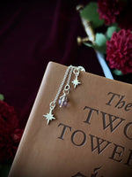 Silver star charms hanging from the top of a leather book with flowers and a sword in the background.