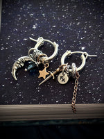 Pair of silver earrings with charms on a dark textured surface